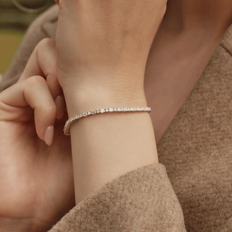 Close-up of a woman’s wrist wearing a slim diamond tennis bracelet, with her hand gently resting near her neck.