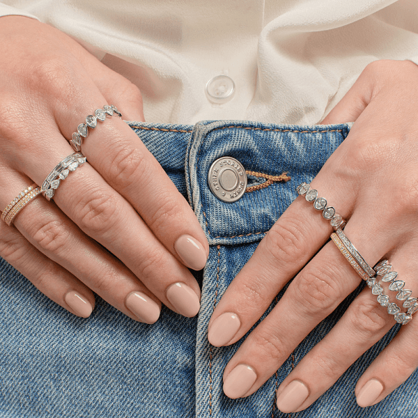 Woman wearing multiple diamond rings on both hands, resting on blue denim jeans with a white shirt.
