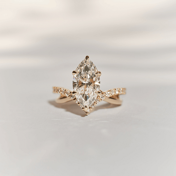Close-up of a marquise-cut diamond engagement ring set in gold, showcasing its brilliance on a soft neutral background.