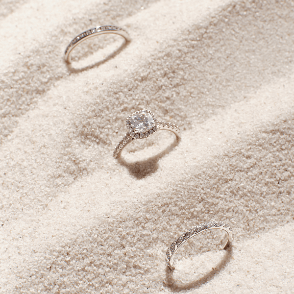 Three diamond rings, including a solitaire engagement ring, displayed on textured sand.