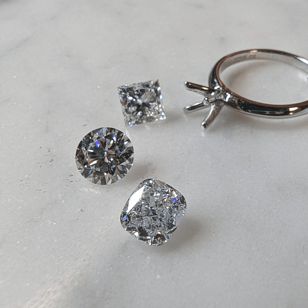 An image depicting loose diamonds of different cuts near a ring base.