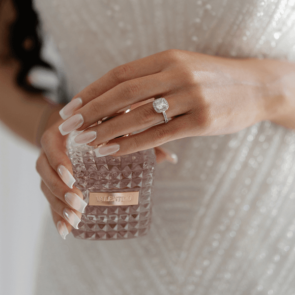 Photo of a bride holding a perfume bottle, showing her diamond engagement ring and elegant bridal manicure.