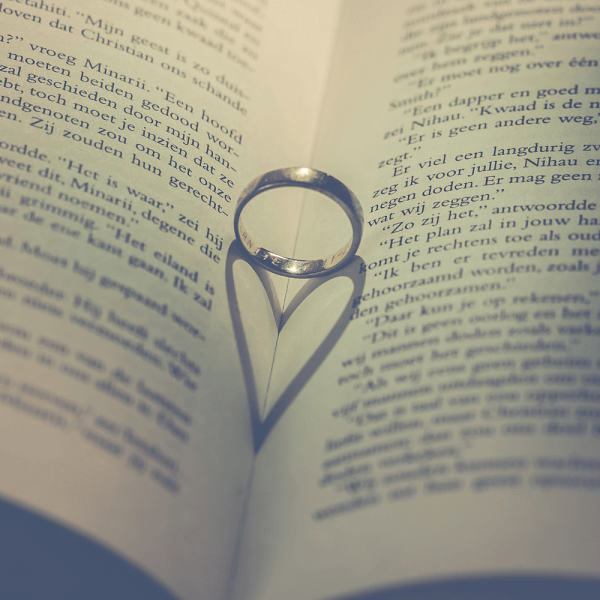 An image featuring an engraved band engagement ring resting on an open book.