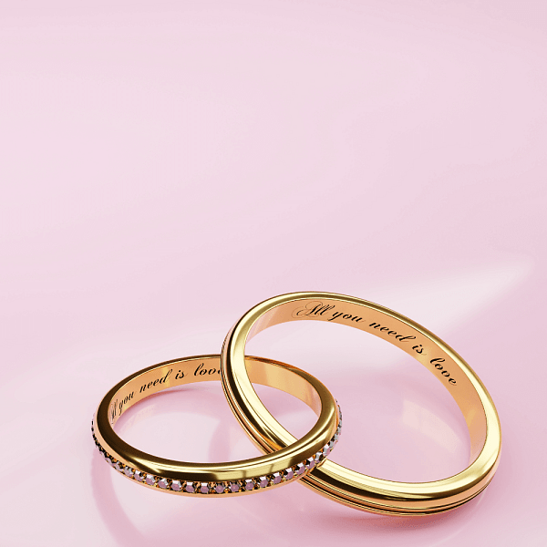 An image showcasing a pair of gold band engagement rings engraved with “all you need is love”, resting on an open book.