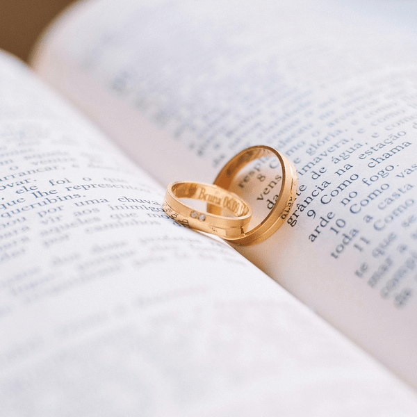 An image featuring a pair of gold band engagement rings, resting on an open book.