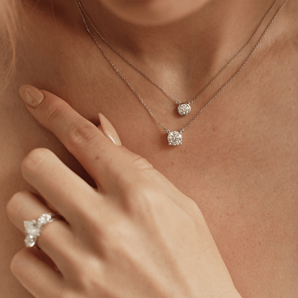 Layered diamond pendant necklaces worn with a diamond ring for styling inspiration.