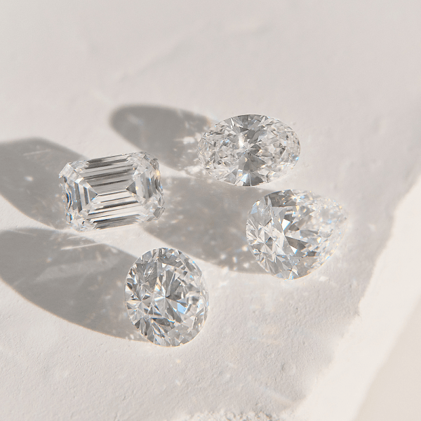 Assorted loose diamonds in different cuts, including round and emerald, displayed on a light surface with soft shadows.