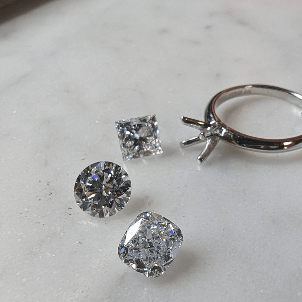 Loose diamonds and an empty ring setting displayed on a marble surface.