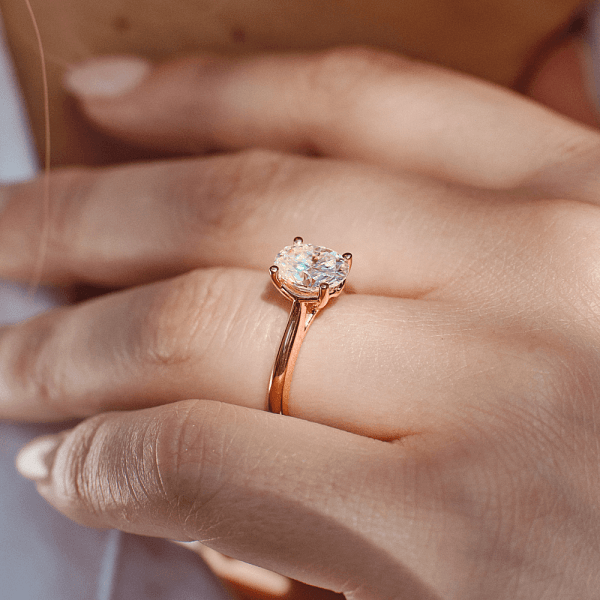 Close-up of a woman’s hand wearing a solitaire diamond engagement ring on a gold band.