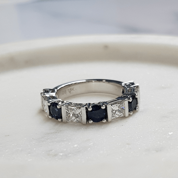 Close-up of a sapphire and diamond ring set in white gold, displayed on a light surface.