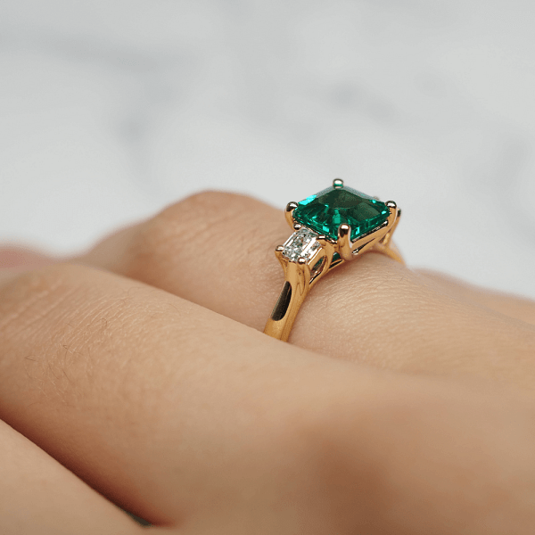 An image of a solitaire ring with an emerald stone, worn on a woman's hand.