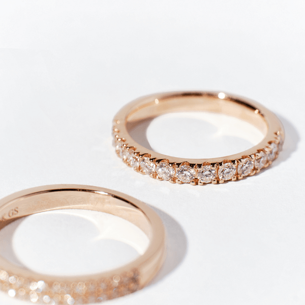 Two rose gold diamond stacker rings on a light surface, featuring a row of small diamonds along the band.
