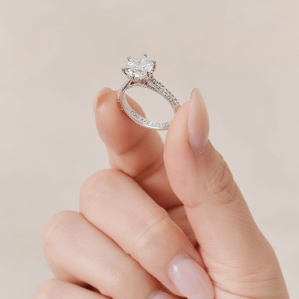 An image of an engraved diamond engagement ring with the inscription “you are loved”.